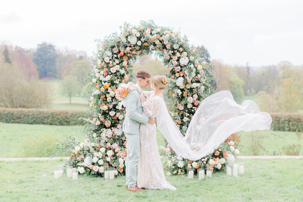 Peach Fuzz Pantone Colour of the Year Wedding flowers luxury florist Flourish and Grace photography by Natalie Stevenson in Paris at Chateau Bouffemont. Flower ceremony arch on lawn and meadow arrangements