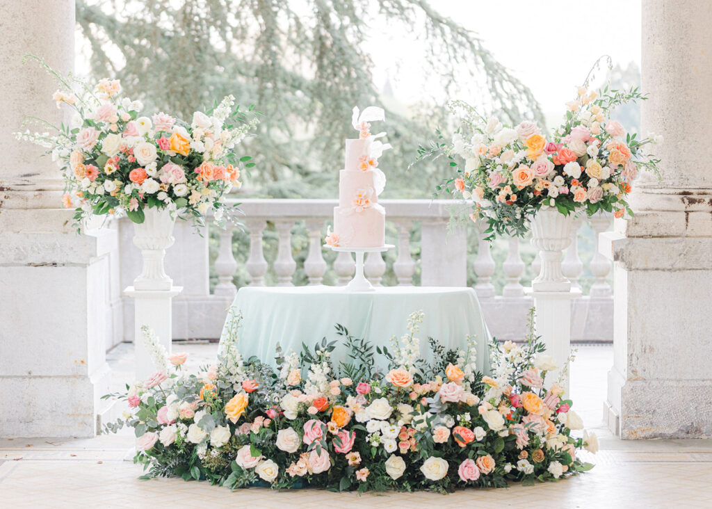 Peach Fuzz Pantone Colour of the Year Wedding flowers luxury florist Flourish and Grace photography by Natalie Stevenson in Paris at Chateau Bouffemont. Cake with urns and flowers meadows on terrace at chateau