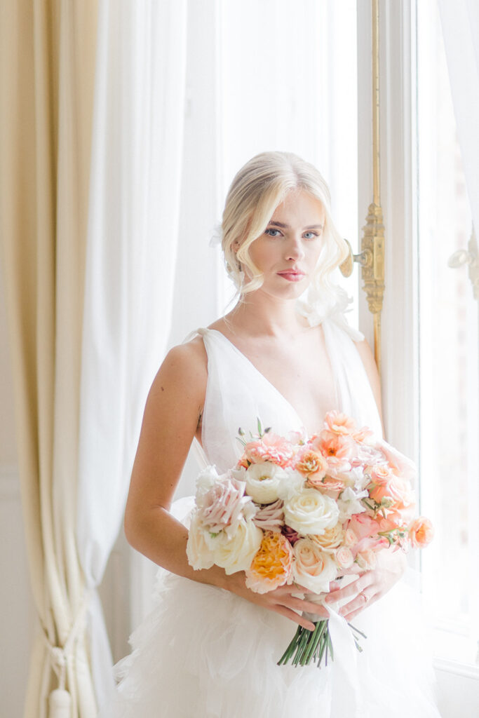 Peach Fuzz Pantone Colour of the Year Wedding flowers luxury florist Flourish and Grace photography by Natalie Stevenson in Paris at Chateau Bouffemont. Bride with peach bouquet in ballroom